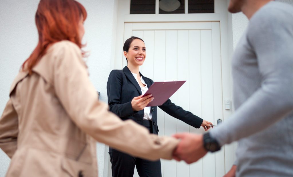 Successful real estate agent near door inviting young couple to enter house for visit